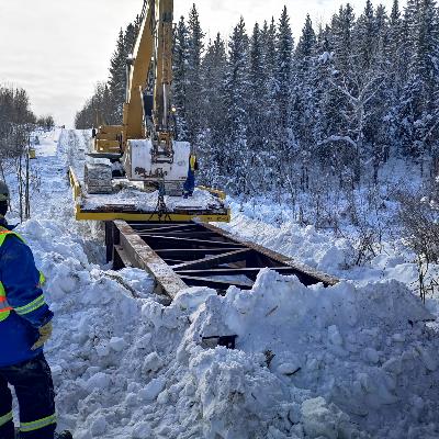 Equipment in snowy area building bridge with employee supervising 