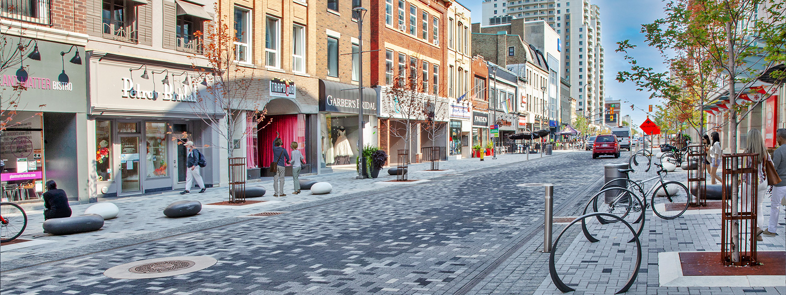 London, Ontario, Dundas Place flexible street rendering. Street is lined with shops, pedestrians, bicycles and vehicles.