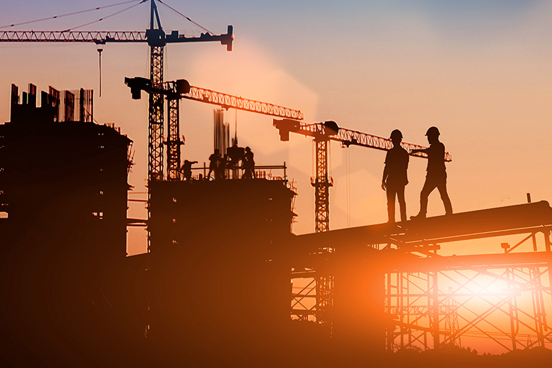 Construction site at sunset with two workers in walking on a beam