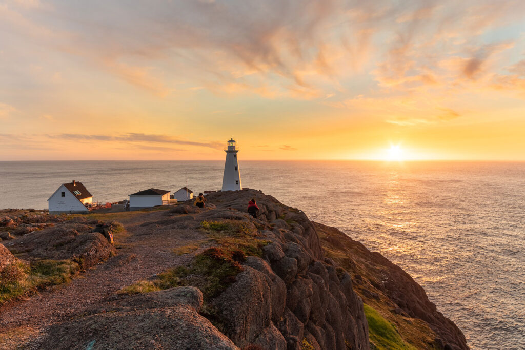 Lighthouse sitting on the edge of a cliff face, overlooking the ocean at sunset