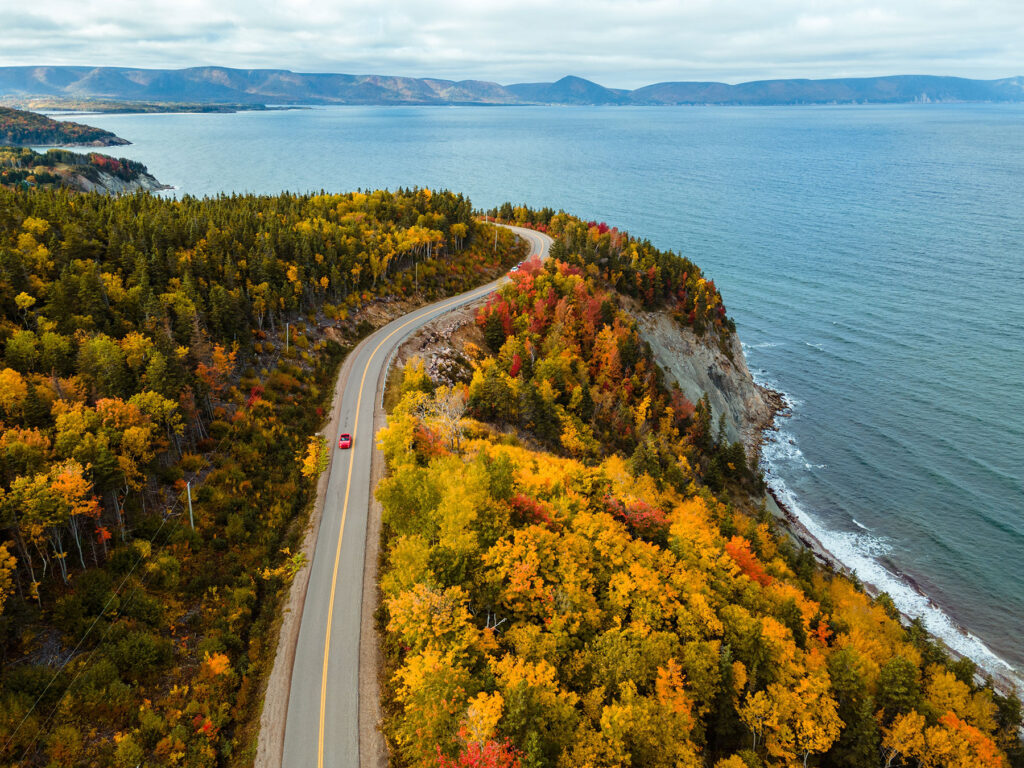 View of a car driving on a winding highway in Cape Breton, Nova Scotia, during the fall