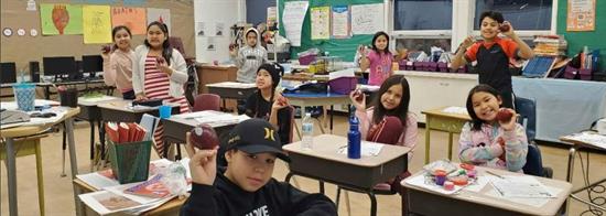 children in a classroom holding up apples while on a nutrition break