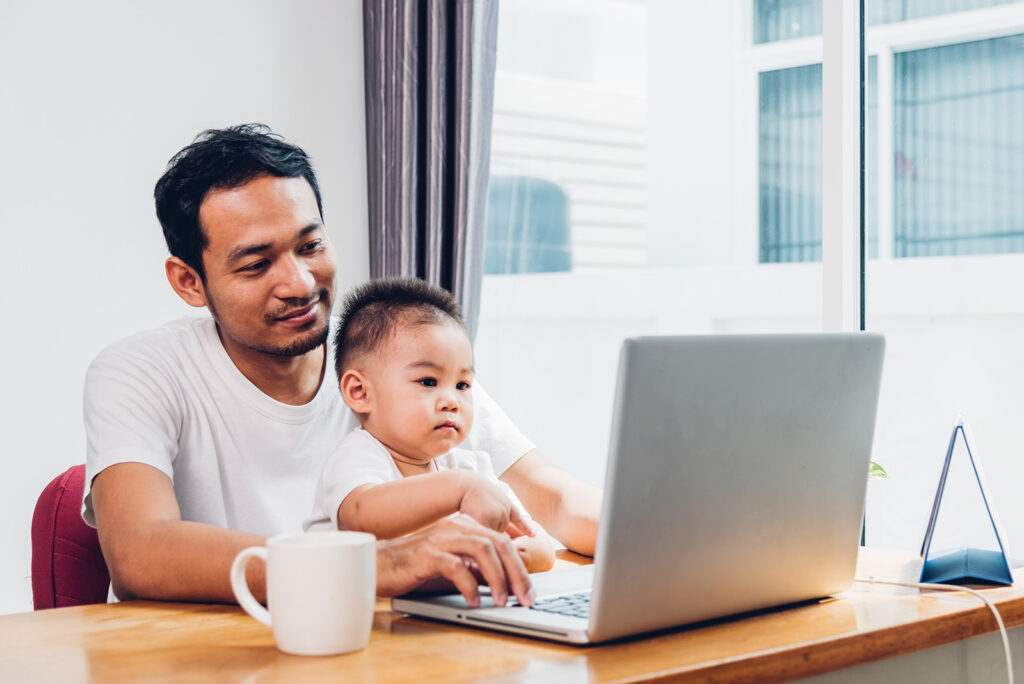 Male holding a baby on his lap while working at a laptop