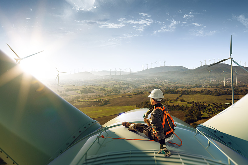 Worker clipped in and sitting on the top of a wind turbine