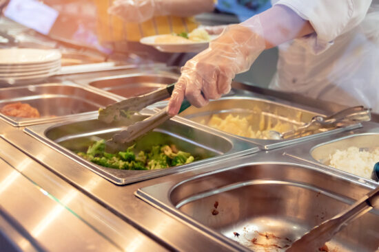 Chef standing behind full service lunch station with assortment of hot foods