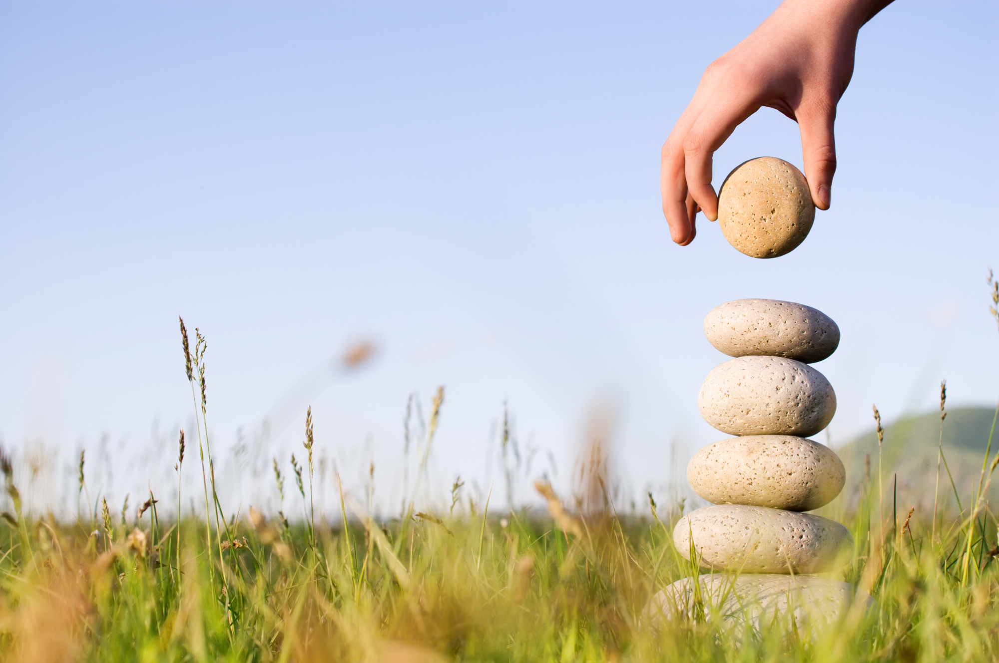 hand placing a stone on a pile of balanced stones