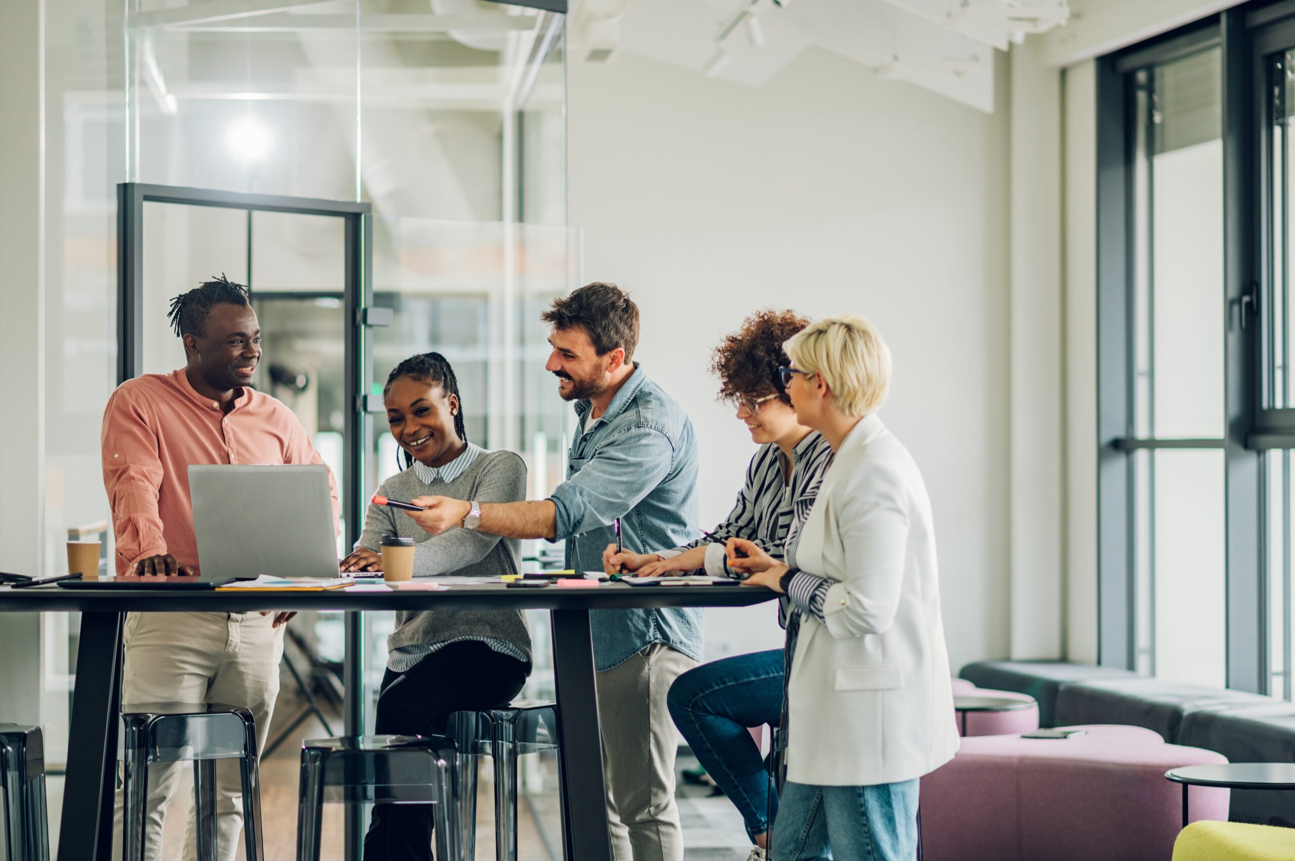 diverse employees stand around a laptop in a meeting